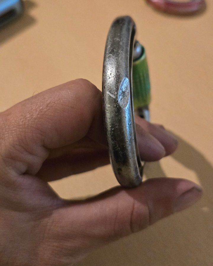 Steel karabiner seen side-on, with a deep gouge cut into the spine and pitting across the surface