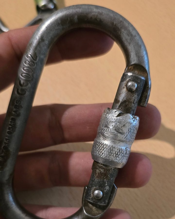 Steel oval screwgate karabiner with a crushed and torn locking sleeve and rust on the gate